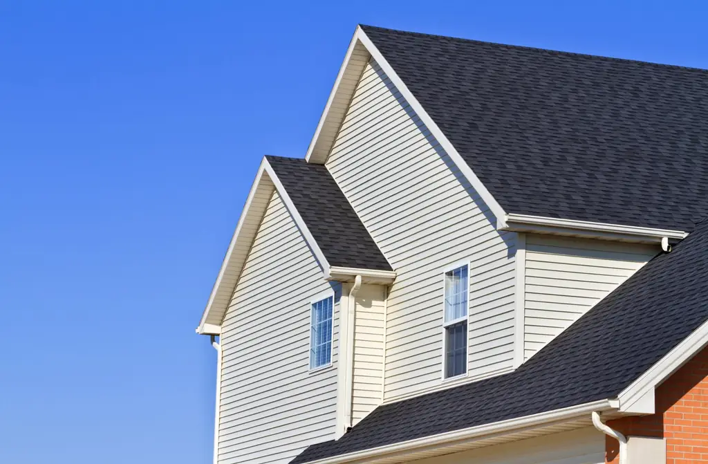 Steep dark shingle roof over cream vinyl siding
